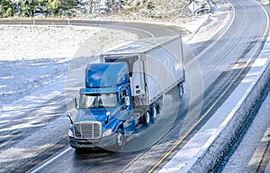 Big rig blue day cab semi truck transporting cargo in reefer semi trailer driving on winter wet road with snow