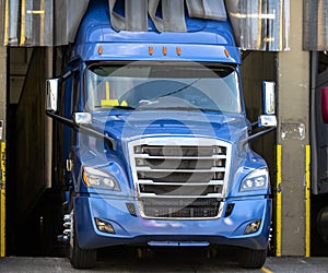 Big rig blue semi truck loading commercial cargo in warehouse dock