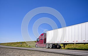 Big rig bonnet long haul diesel semi truck transporting commercial cargo in dry van semi trailer running on the local narrow road