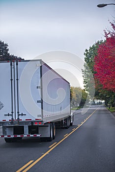 Big rig bonnet semi truck with dry van semi trailer running on autumn colorful road