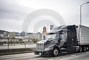 Big rig bonnet semi truck with grille guard transporting frozen cargo in refrigerator semi trailer driving on the city overpass