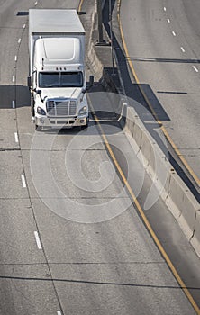 Big rig bonnet semi truck transporting cargo in dry van semi trailer driving on the left line on wide highway in sunny day
