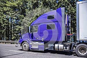 Big rig bonnet semi truck in ultramarine color transporting cargo in dry van semi trailer running on the highway road