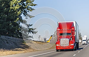 Big rig bright red classic American idol semi truck with reefer semi trailer driving on the straight highway in sunny day