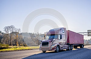 Big rig brown semi truck transporting container on wide highway with trees on the side