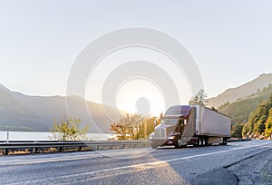 Big rig burgundy semi truck transporting commercial cargo in refrigerator semi trailer driving on the road along Columbia River