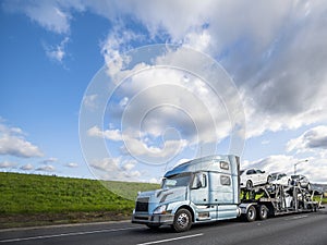 Big rig car hauler semi truck transporting cars on the special semi trailer driving on the flat road with green hill