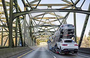 Big rig car hauler semi truck transporting cars on the trailer and driving on the truss arched bridge