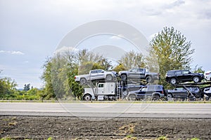 Big rig car hauler semi truck transporting cars on two level semi trailer running on the divided highway road