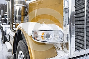 Big rig classic gold semi truck with chrome accessories standing on the winter parking lot with snow and ice