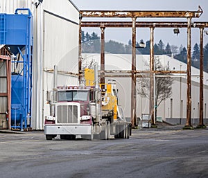 Big rig classic semi truck with step deck semi trailer transporting equipment to warehouse