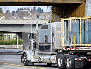 Big rig classic semi truck transporting glass sheets in wood boxes on flat bed semi trailer turning under the bridge