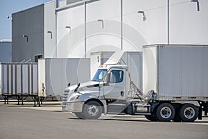 Big rig commercial day cab semi truck with dry van semi trailer loading cargo at warehouse dock for the next delivery