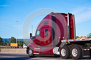 Big rig dark red semi truck tractor driving with flat bed trailer on the road