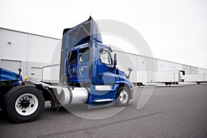 Big rig day cab blue semi truck driving to warehouse dock for pi