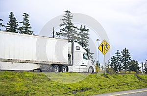 Big rig day cab semi truck with bulk semi trailer turning on the highway entrance with green trees on the sides