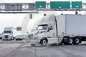 Big rig day cab semi truck with semi trailer turning on the crossroad intersection with traffic lights