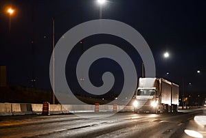 Big rig day cab semi truck transporting cargo in two semi trailers running on the wet after rain highway road at dark night time