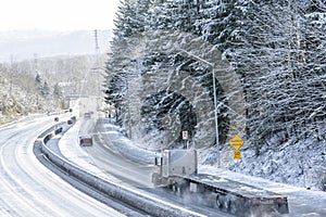 Big rig gray classic semi truck with flat bed semi trailer driving on the winter snowy highway to warehouse for loading cargo