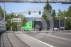 Big rig green industrial grade semi truck with black covered semi trailer turning on the city crossroad with traffic lights