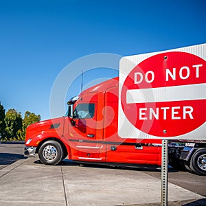 Big rig industrial red semi truck with semi trailer turning on the local road with do not enter sign