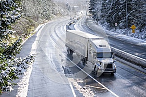 Big rig semi truck with semi trailer driving on winter snowy highway with wet melting snow surface