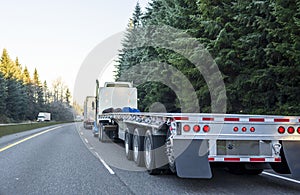 Big rig long haul semi truck with empty flat bed semi trailer running on the winter road in convoy with another semi trucks photo