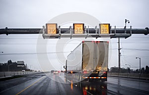 Big rig long haul semi truck transporting commercial cargo in dry van semi trailer running on twilight wet road at raining weather