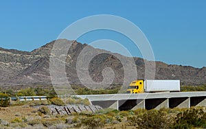 Big rig long haul semi truck with two flat bed semi trailers transporting on the winding road with bridge around the mountain rock