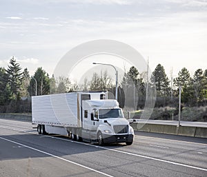 Big rig low cab white semi truck transporting cargo in refrigerated semi trailer running for delivery on the wide divided highway