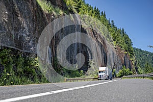 Big rig quality freight semi truck transporting cargo in bulk semi trailer driving on the scenic winding mountain road going