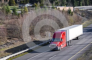 Big rig red semi truck with dry van semi trailer transporting cargo running on the highway road intersection with one way traffic