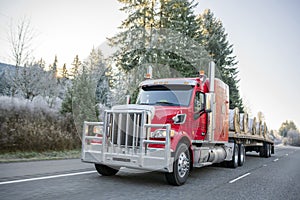 Big rig red semi truck with powerful grille guard transporting cargo on flat bed semi trailer driving on winter road