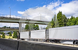 Big rig semi truck auto train running with three dry van semi trailers going under the overpass trestle road