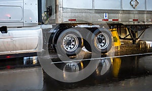 Big rig semi truck with a chassis with wheels carries cargo in a dry van semi trailer moving on a wet road slippery from rain