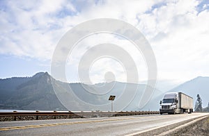 Big rig semi truck with dry van semi trailer transporting carg driving along the river in Columbia Gorge area