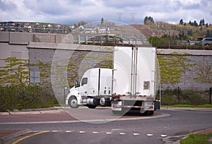 Big rig semi truck with dry van semi trailer turning on the circular intersection of road under the bridge