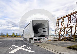 Big rig semi truck with empty refrigerator semi trailer with open door standing on the road shoulder in industrial warehouse area