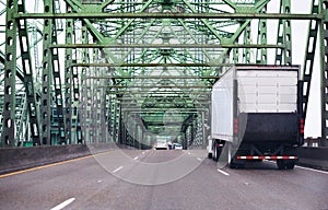 Big rig semi truck with lifting back door unit going highway along truss bridge