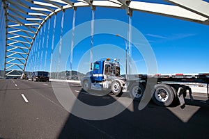Big rig semi truck with long flat bed trailer running on arched