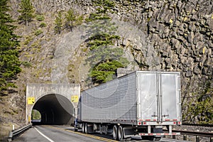 Big rig semi truck with refrigerator semi trailer moving on the road with tunnel through the rock
