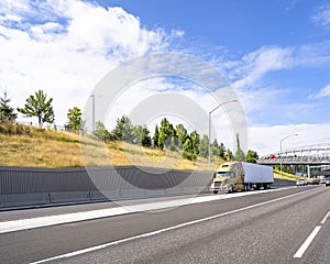 Big rig semi truck with refrigerator semi trailer transporting cargo driving on the wide highway with bridge and wall on the