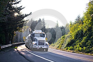 Big rig semi truck with tank trailers on winding road in forest