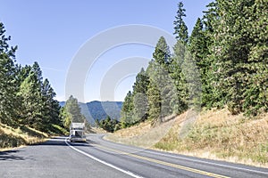 Big rig semi truck tractor transporting cargo climbing uphill on the winding mountain road with forest on the sides