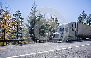 Big rig semi truck transporting cargo in refrigerated semi trailer going downhill on the road with autumn trees in Columbia Gorge