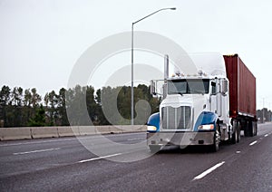 Big rig semi truck transporting container on straight wide highway in raining weather