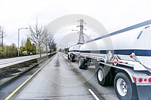 Big rig semi truck transporting fuel in two tank semi trailers driving on straight divided road