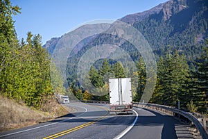 Big rig semi trucks with semi trailers drive towards each other on the winding mountain road