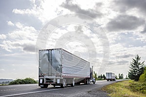 Big rig semi trucks transporting cargo in semi trailers running on the eveing local road