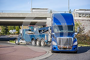 Big rig tow truck towing broken blue big rig semi truck tractor going under the bridge